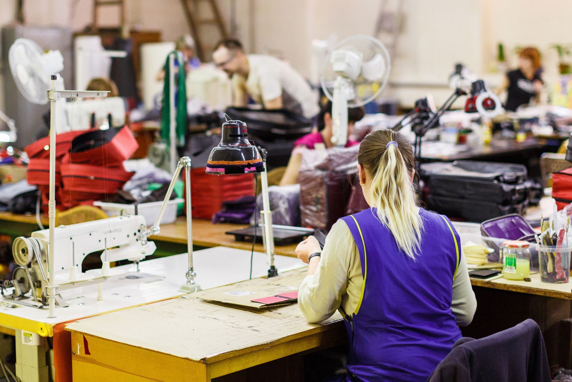Person working at a sewing machine in a busy tailor workshop with fabric and tools scattered around