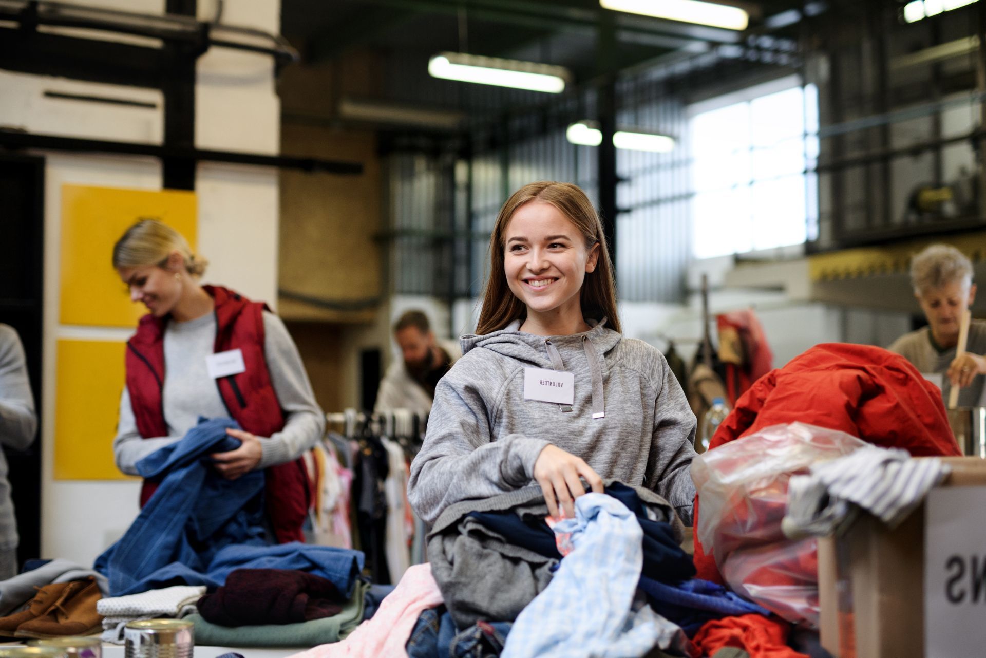 Volunteers sorting through donated clothing in a brightly lit warehouse.