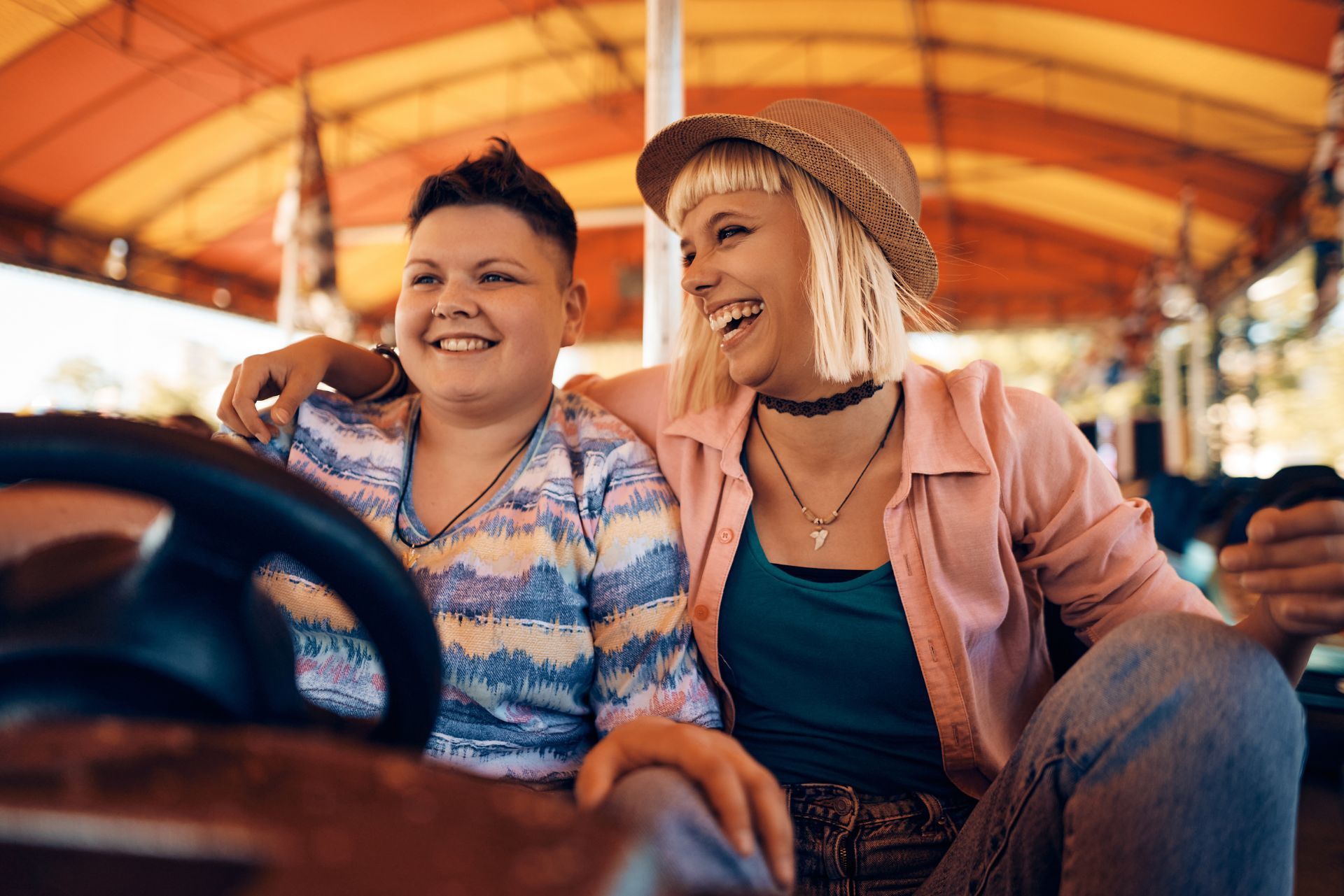 Two people sitting in a bumper car at an amusement park, both smiling and looking to the side.