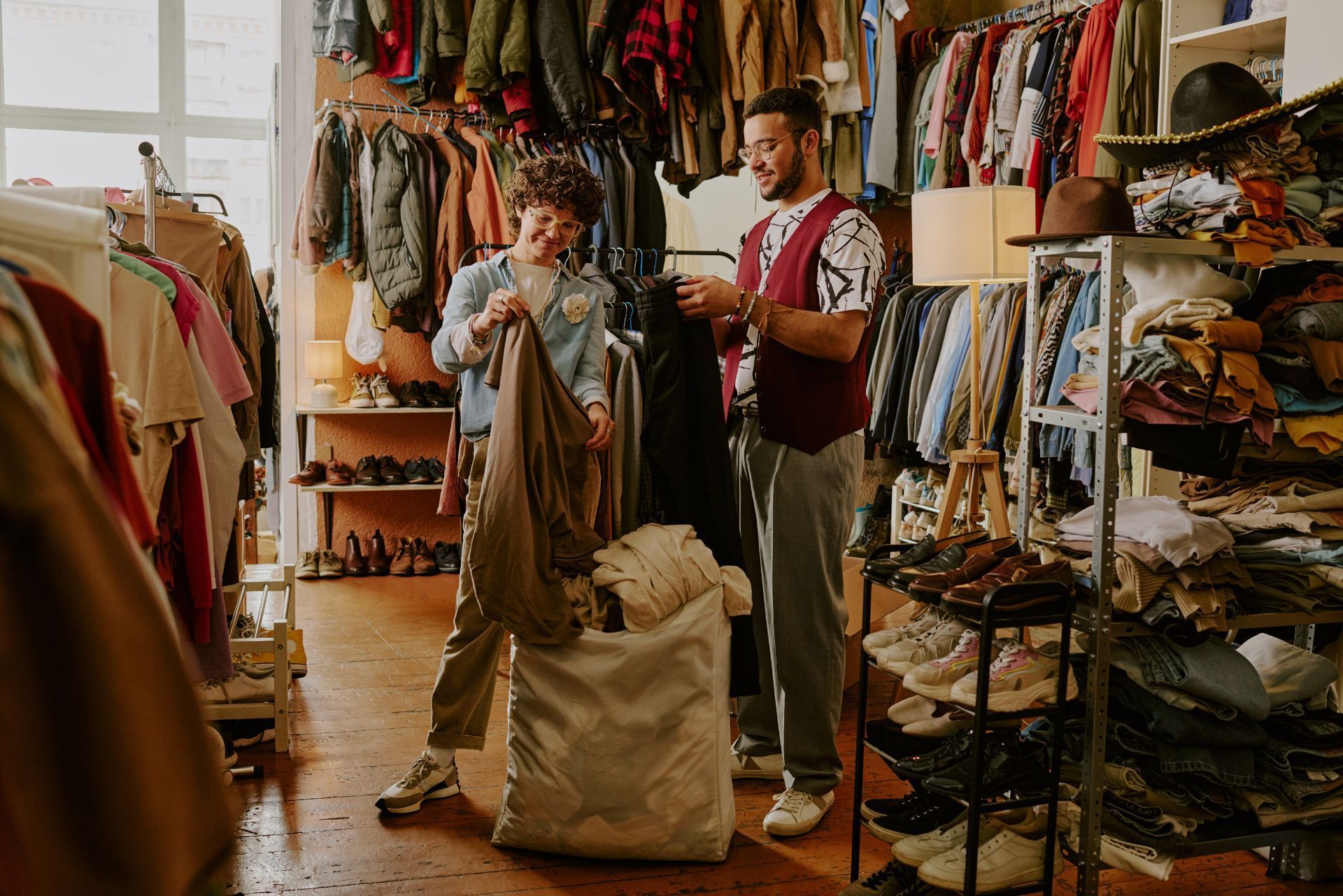 Two people sorting clothes in a crowded vintage shop filled with racks and shelves of garments