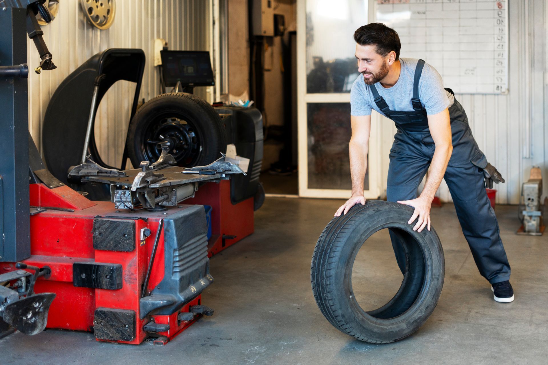 Mechanic rolling a tire in an auto garage beside a red tire machine