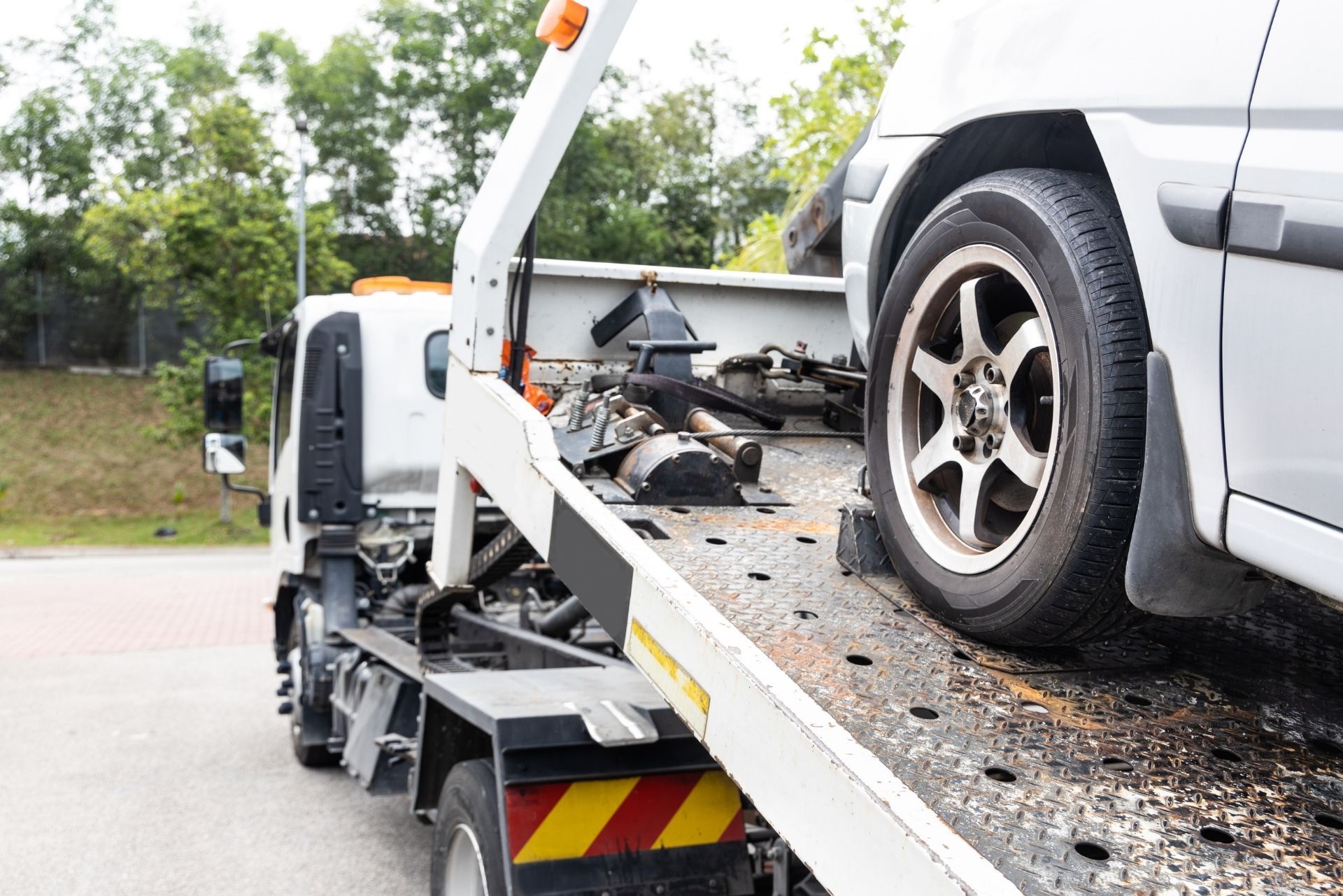 Tow truck carrying a silver SUV on a flatbed beside a road