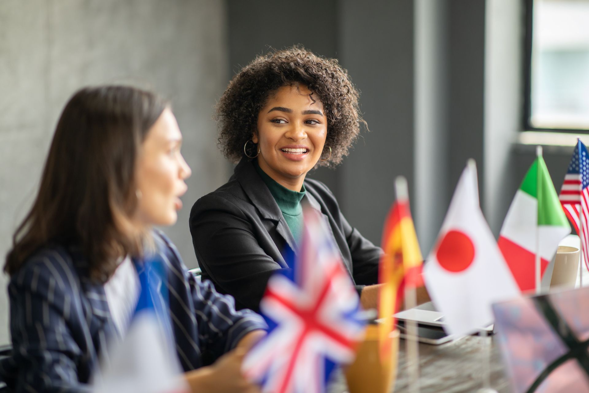People in a meeting with small international flags on the table, one woman smiling and speaking