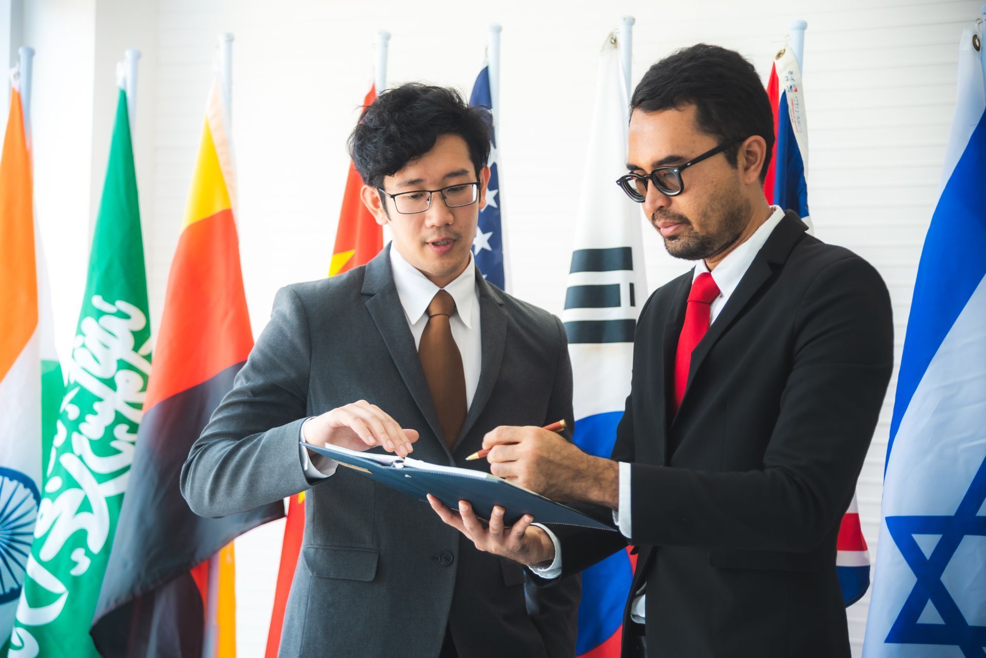 Two suited professionals reviewing a document in front of international flags