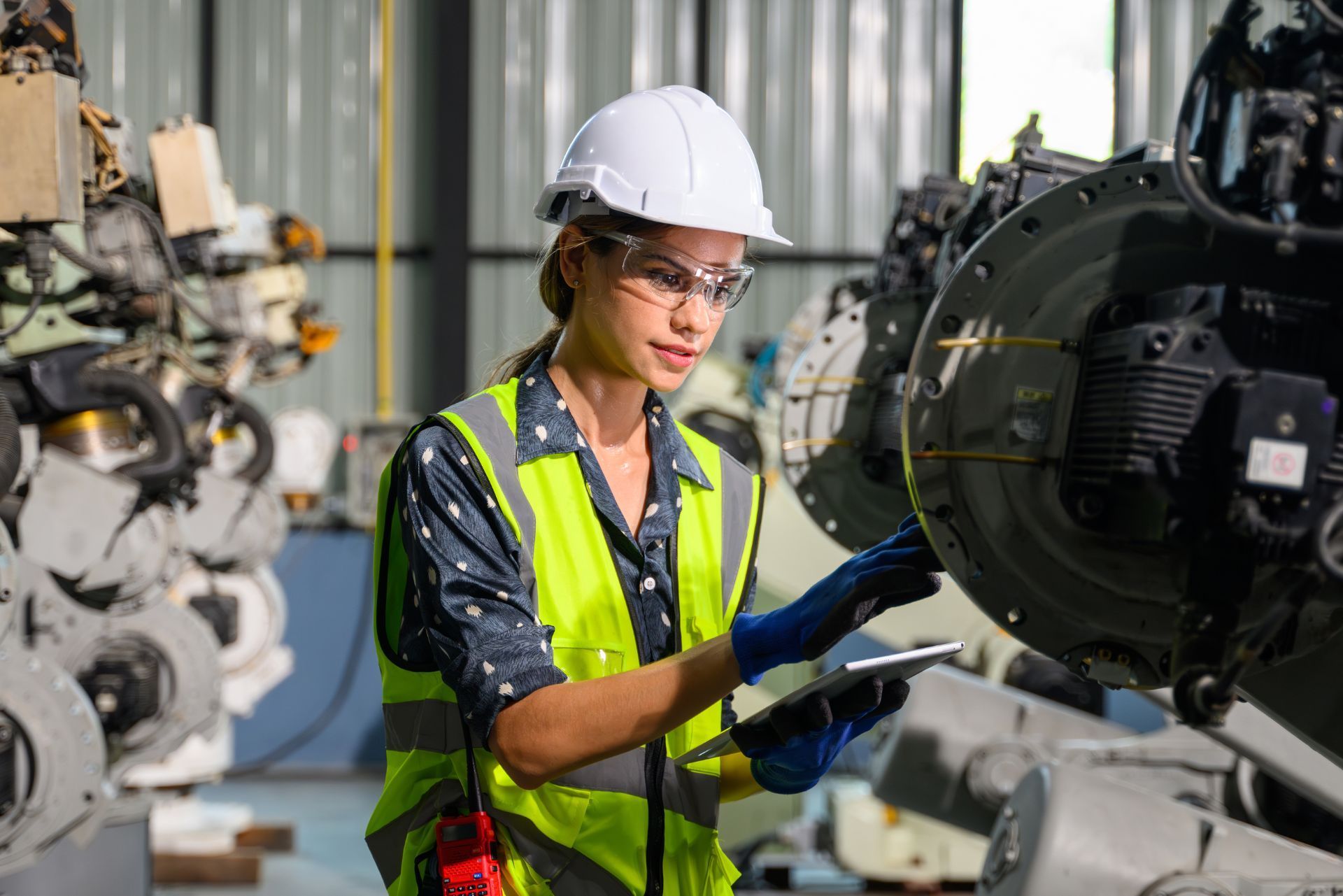 Engineer in hard hat and safety vest inspecting machinery in an industrial workshop