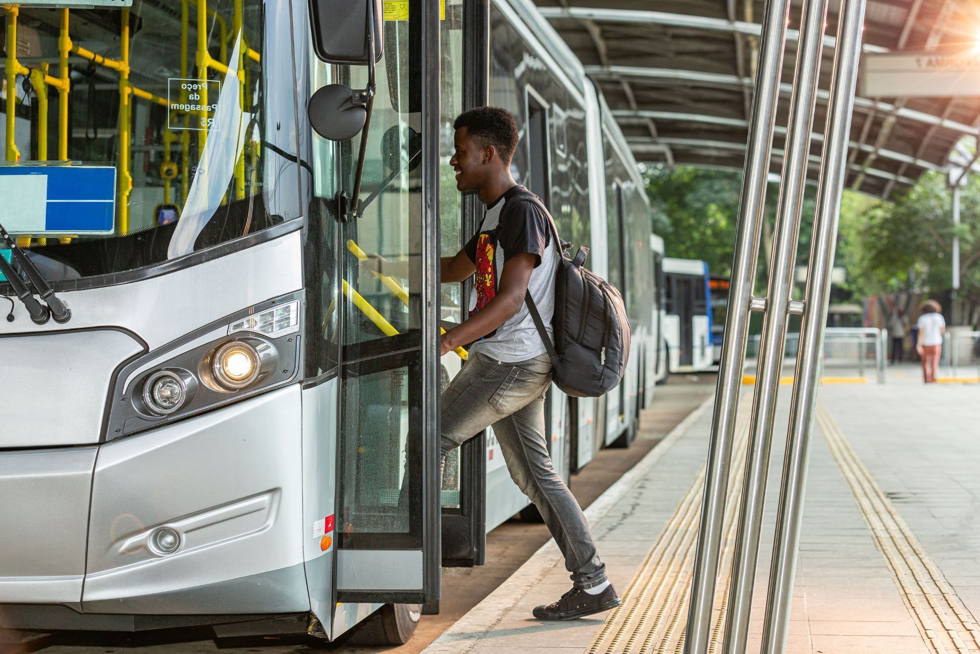 A person with a backpack boarding a silver bus at a modern transit station.