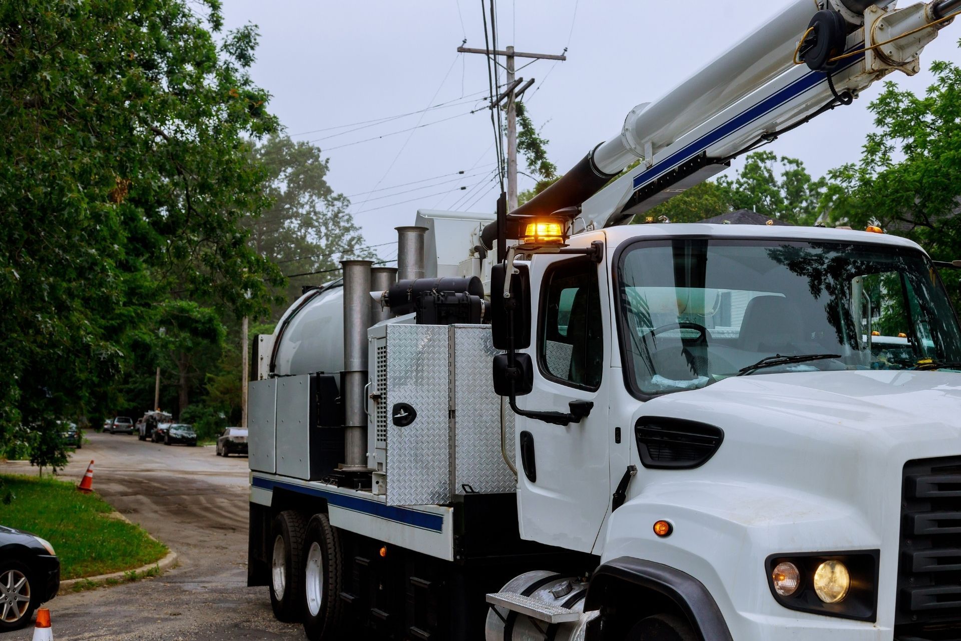 White utility truck with boom lift parked on a tree-lined street after rain