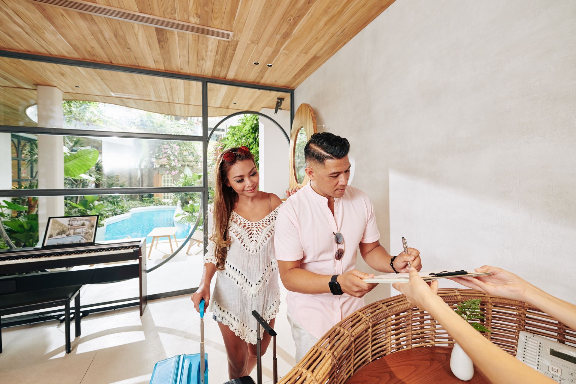 Couple signing a document at a bright outdoor resort reception desk with pool view