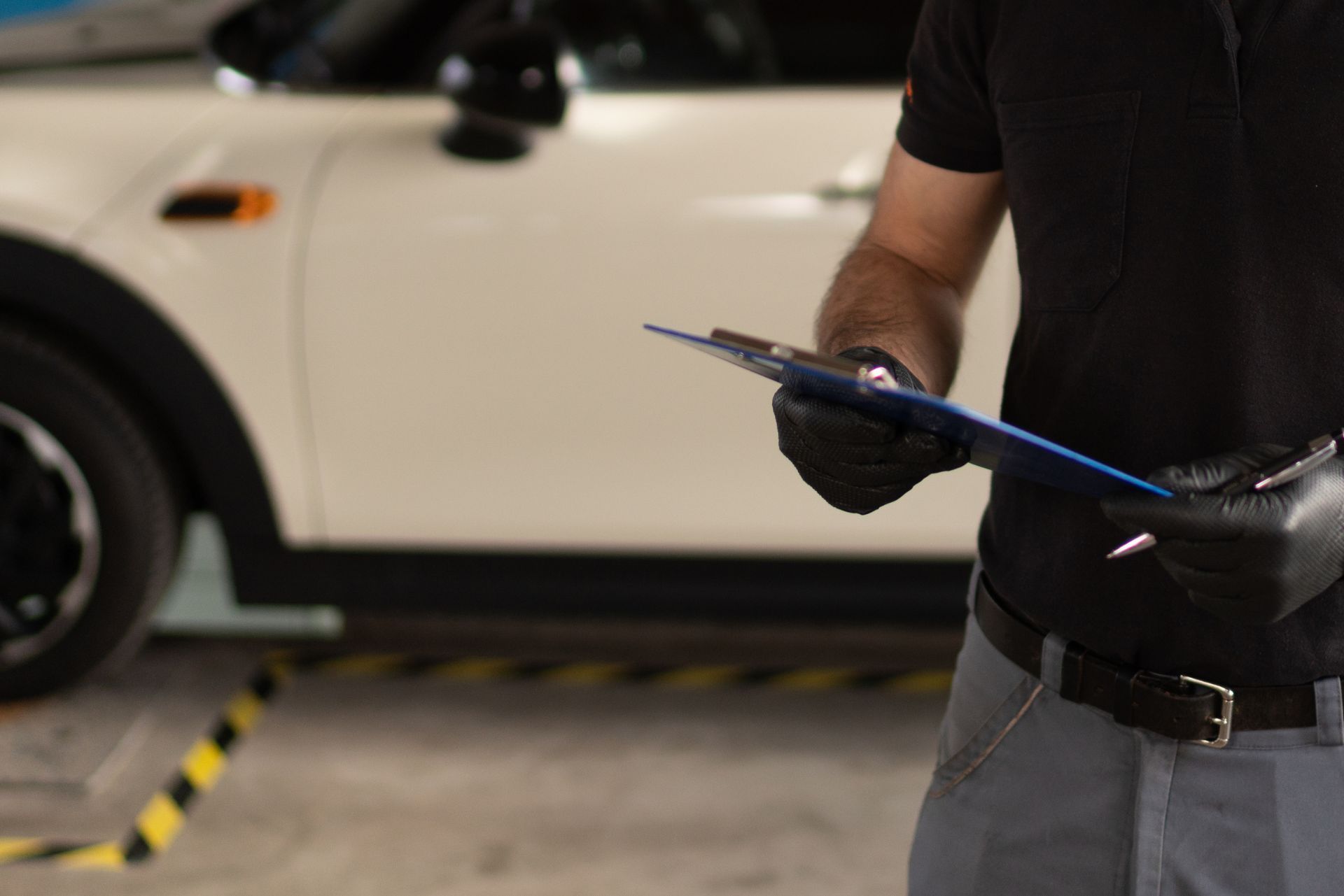Mechanic in black gloves inspecting a tablet beside a white car in a garage