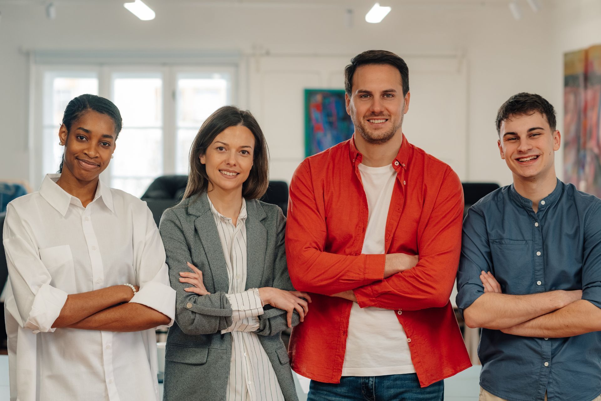 Four colleagues standing with arms crossed in a bright office, smiling at the camera.