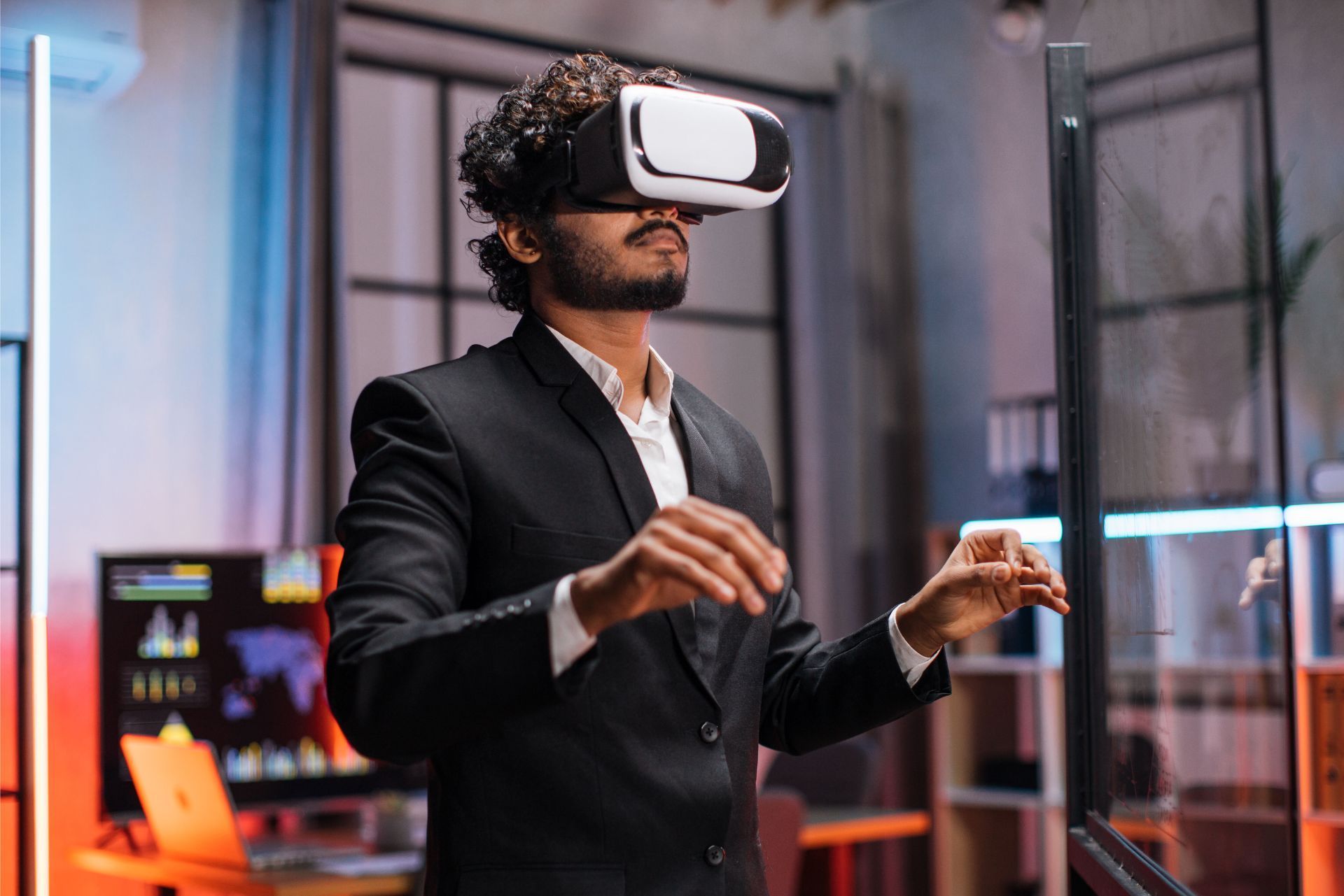 Person in a black suit wearing a VR headset, reaching out in a modern office.