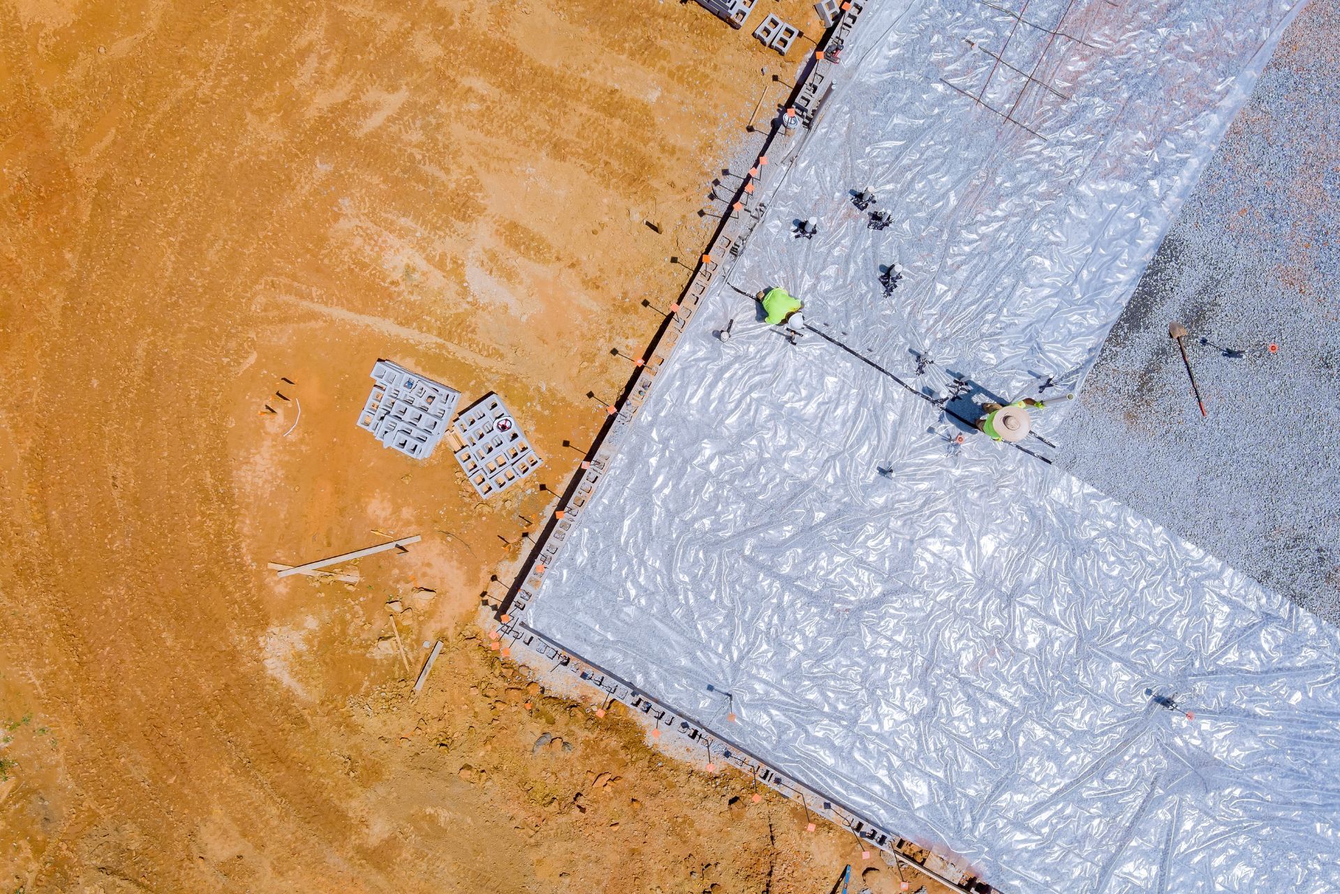 Aerial view of workers on a white-roofed building beside orange dirt ground