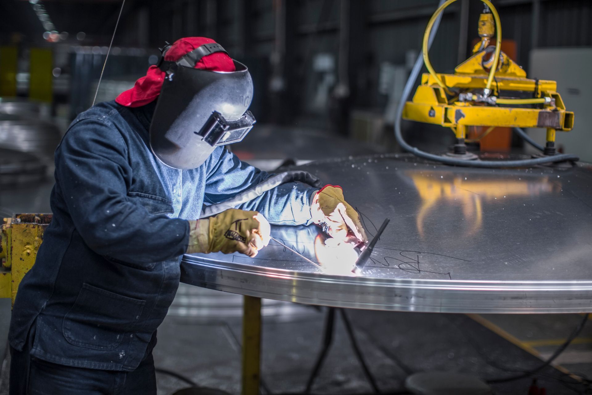 Welder in protective gear sparks metal welding beside a yellow robotic arm in an industrial workshop