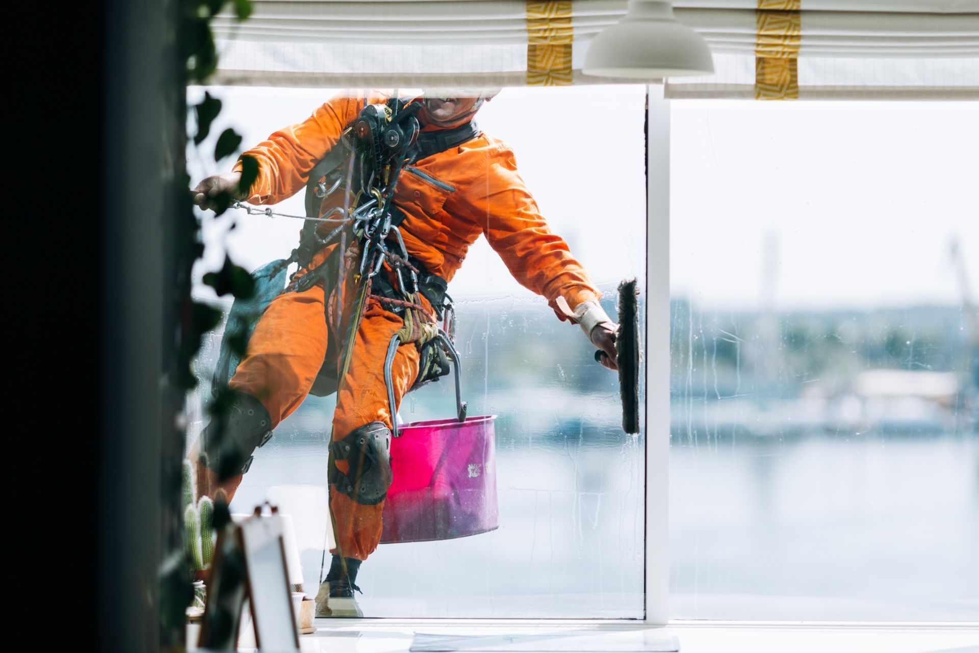 Worker in orange rain gear opening a glass door, holding a pink bag in a snowy setting