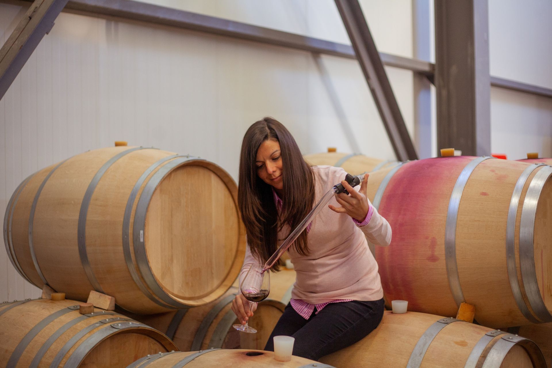 Woman posing among wooden wine barrels in a winery cellar