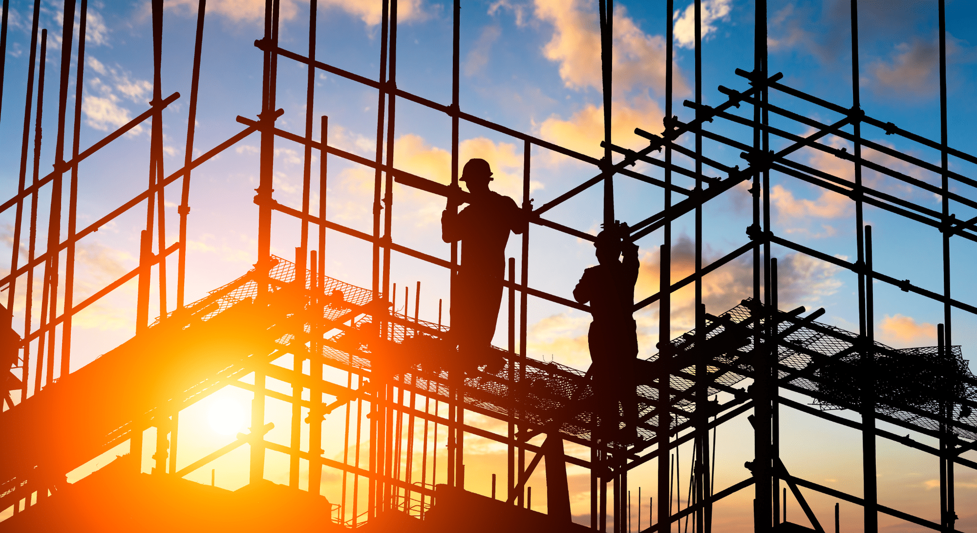 Workers on scaffolding at sunset, silhouetted against a bright orange sky.