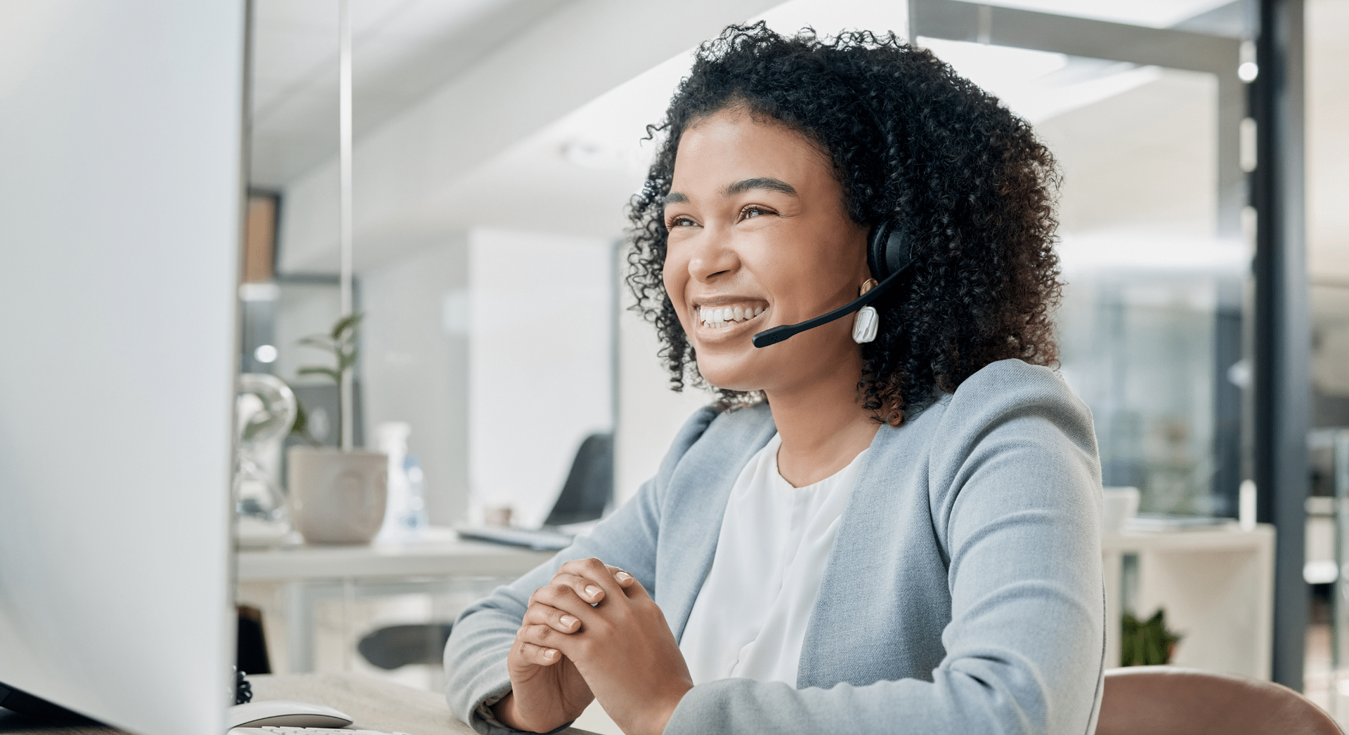 Smiling customer service agent wearing a headset at a desk in a bright office