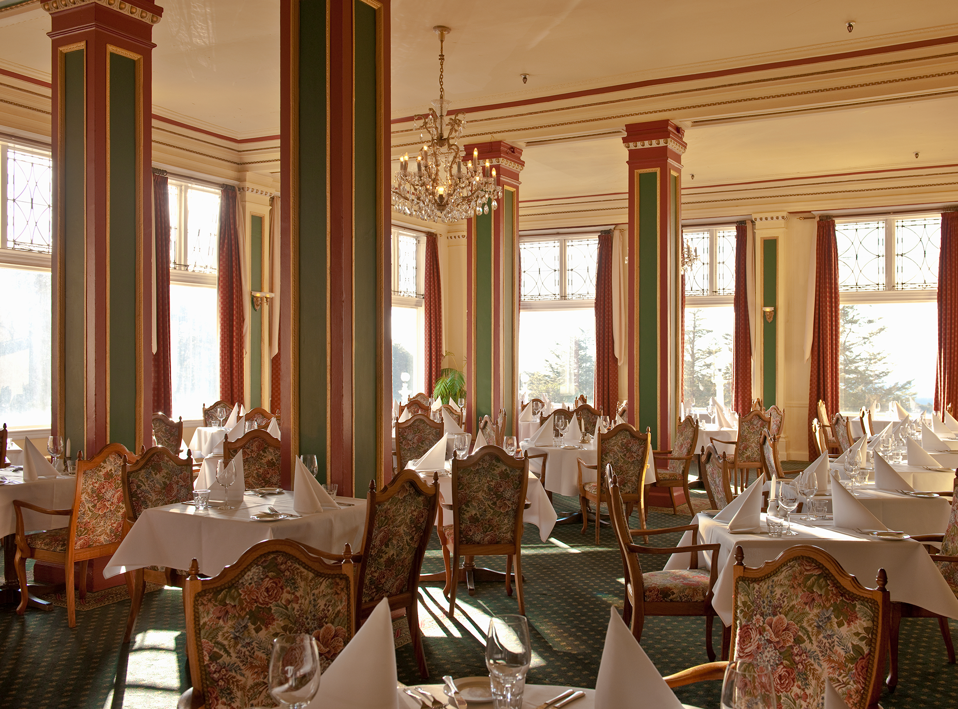 Elegant dining room with white tablecloths, ornate chairs, and sunlit windows overlooking a bright view