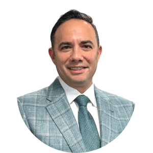 Headshot of a smiling person in a light blue plaid suit and teal tie on a white background