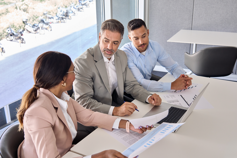 Three coworkers in a bright office reviewing charts around a conference table