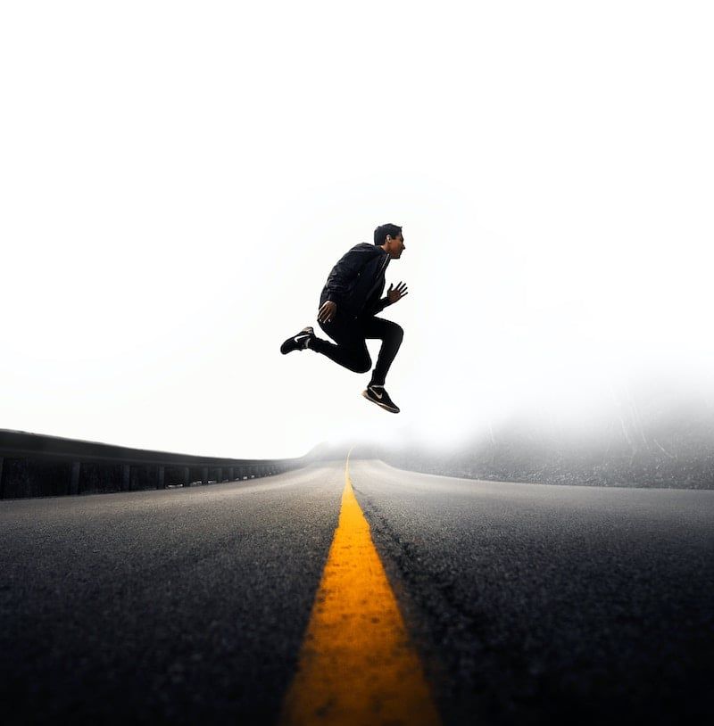 Person leaping above a road’s yellow center line in a foggy, dramatic scene