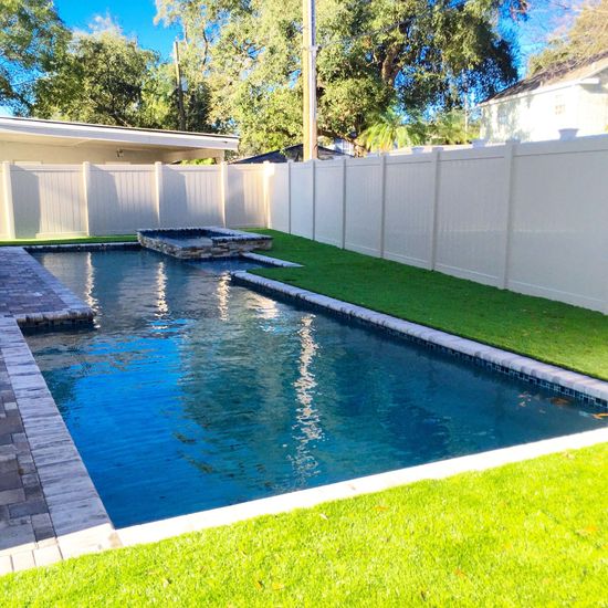 Backyard pool with white fence, artificial turf, and a stone deck.