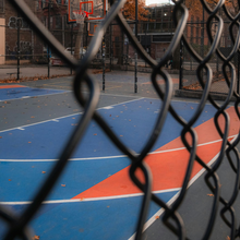 Basketball court behind a black chain-link fence, with blue and orange painted surface.