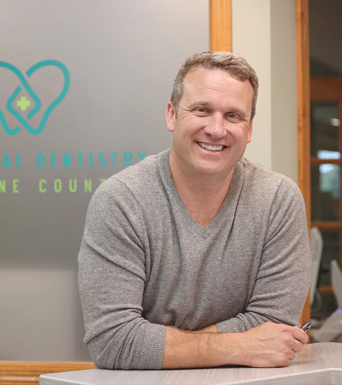 Smiling man in a gray sweater leaning on a counter in an office setting
