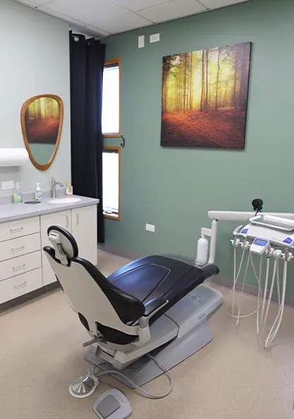 Dental exam room with a reclined chair, sink, and framed wall art on green walls