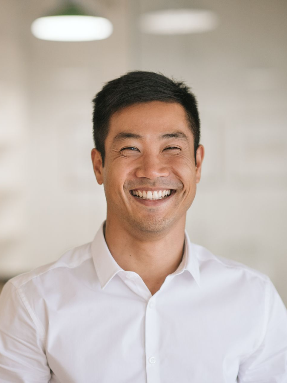 Smiling man in a white shirt standing indoors against a softly blurred background