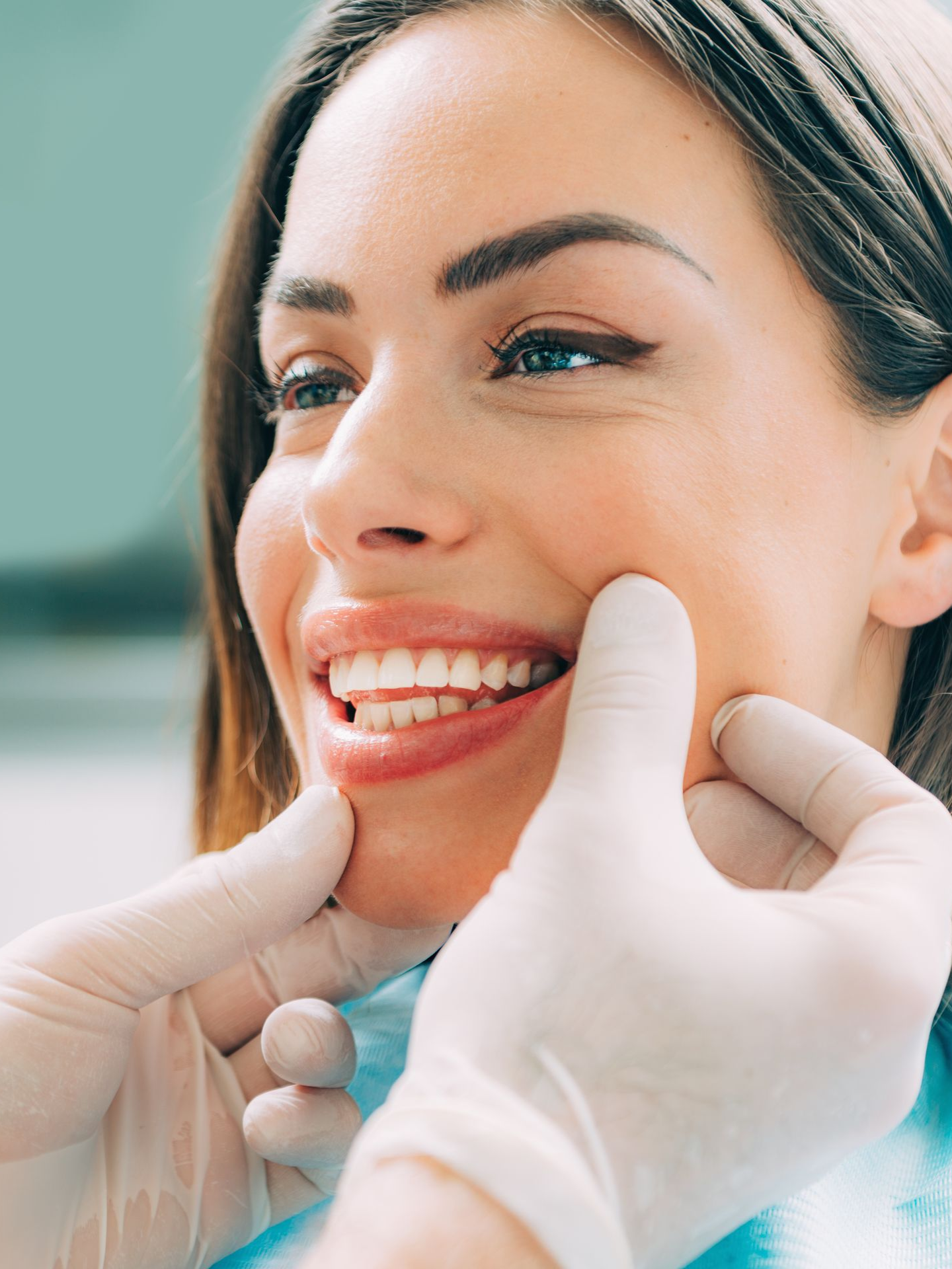 Gloved hands examining a smiling patient’s teeth during a dental checkup