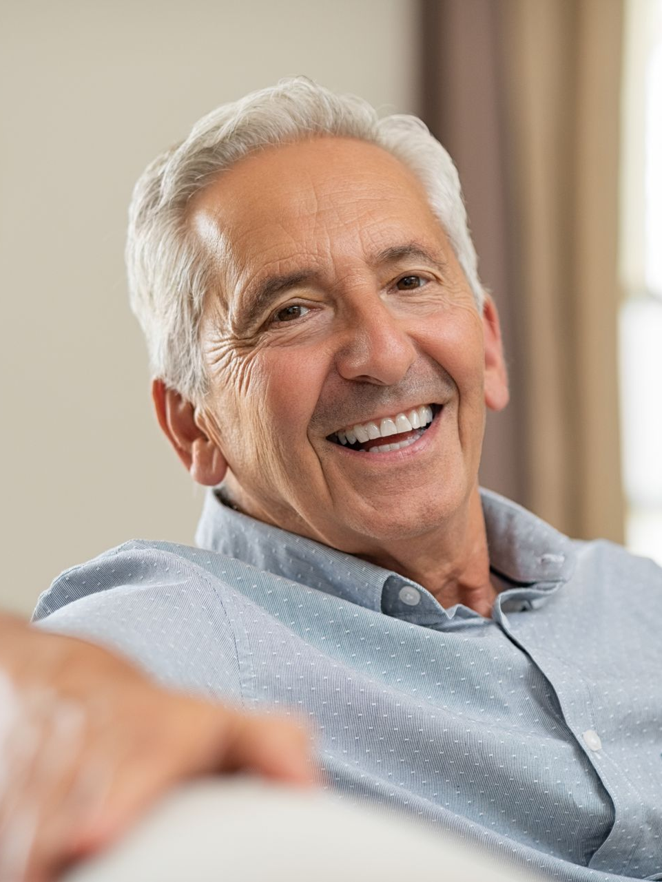 Smiling man in a light blue shirt sitting indoors on a couch