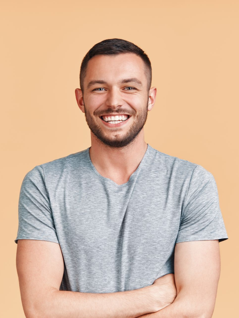 Smiling person in a gray T-shirt with folded arms against a peach background
