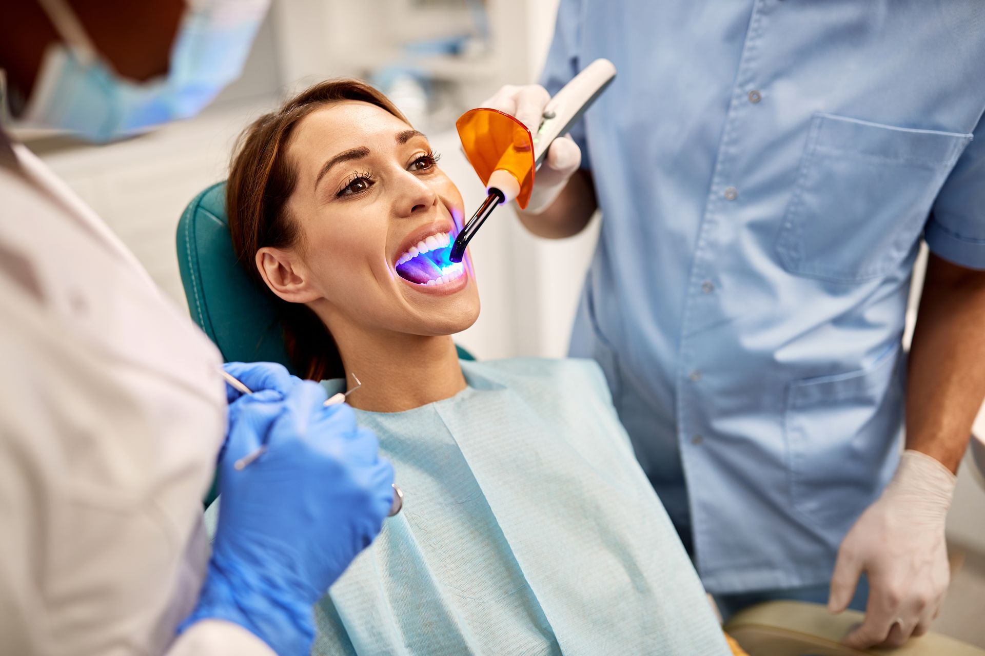 Patient in dental chair while a dentist uses a curing light during treatment