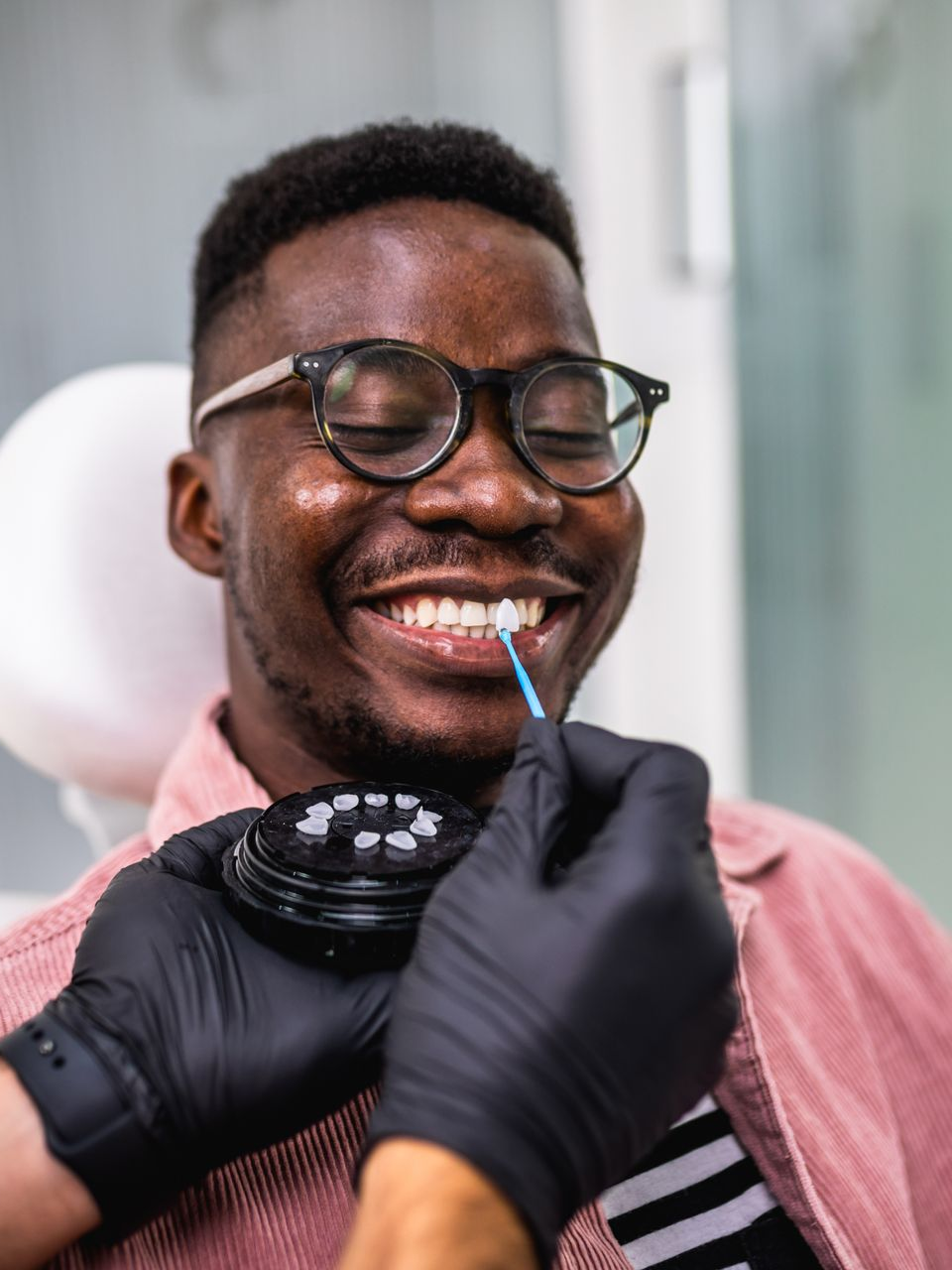 Person smiling during a dental cleaning, with gloved hands using a toothbrush in a clinic.