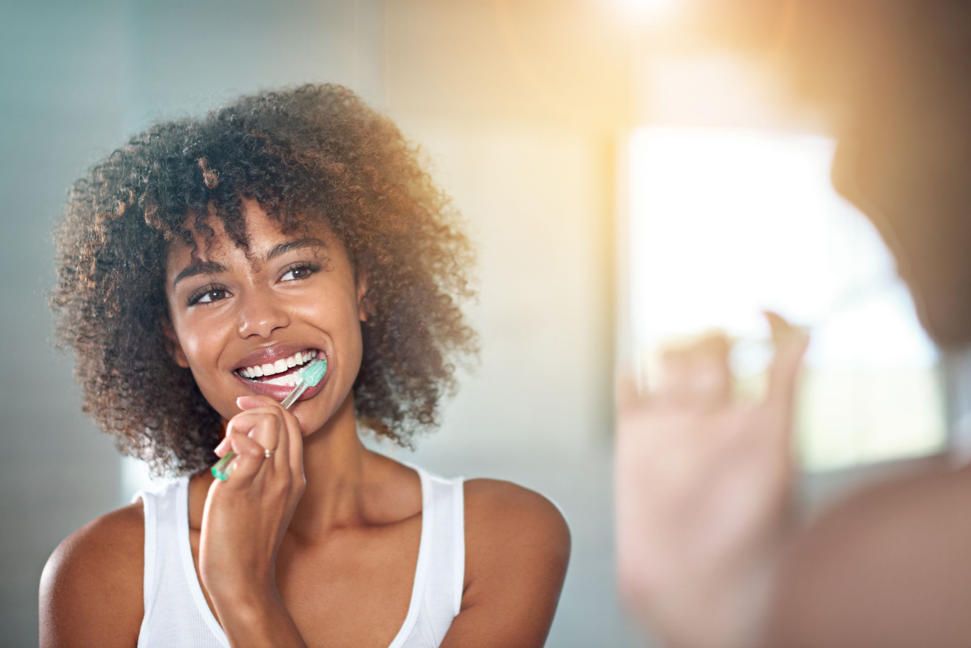 Smiling person brushing teeth in a bright bathroom mirror