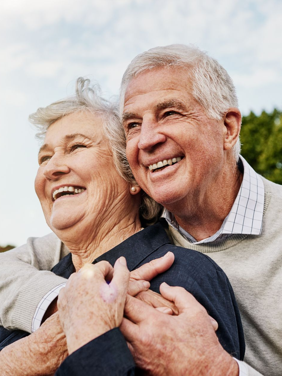 Smiling older couple embracing outdoors under a bright sky