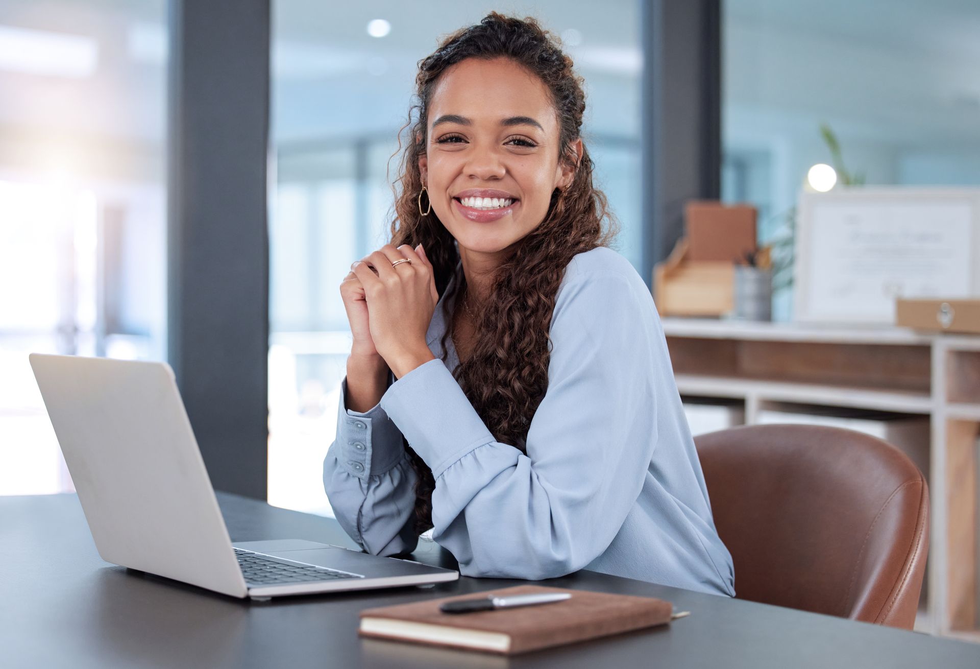 Smiling woman seated at a desk with a laptop in a bright office