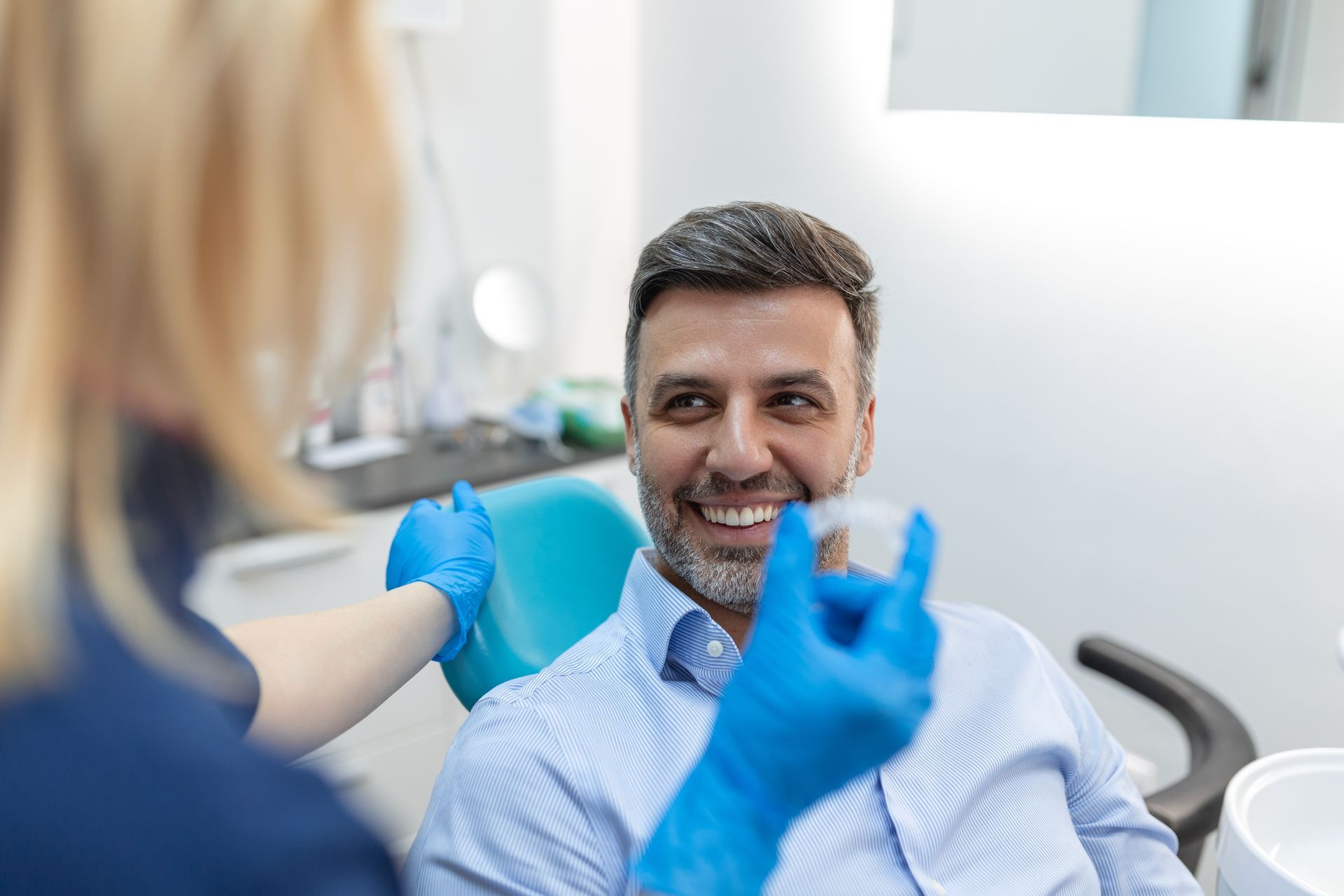 Dentist wearing blue gloves examines a smiling patient in a dental chair