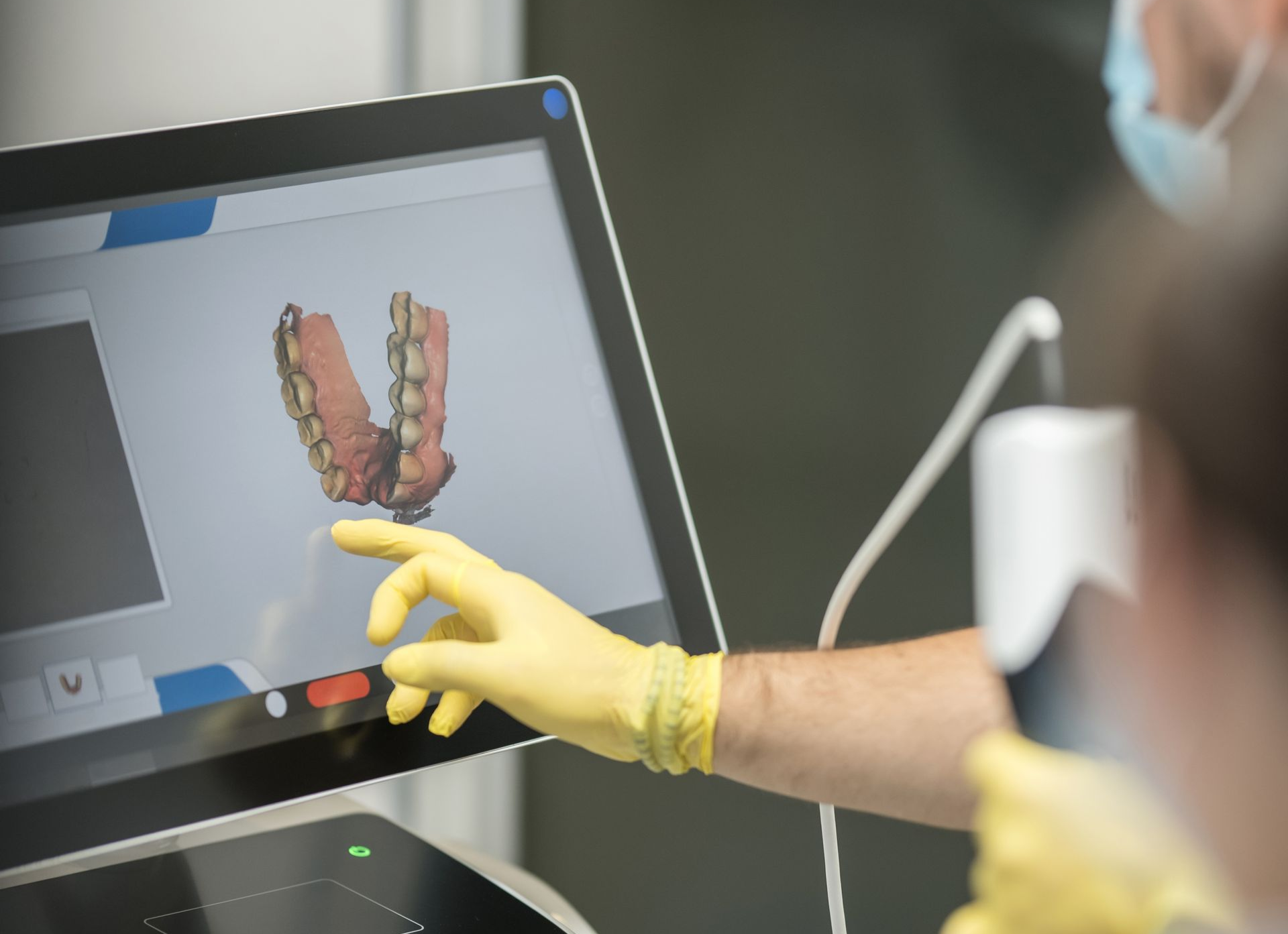 Gloved hand points at a dental scan on a touchscreen monitor in a clinic