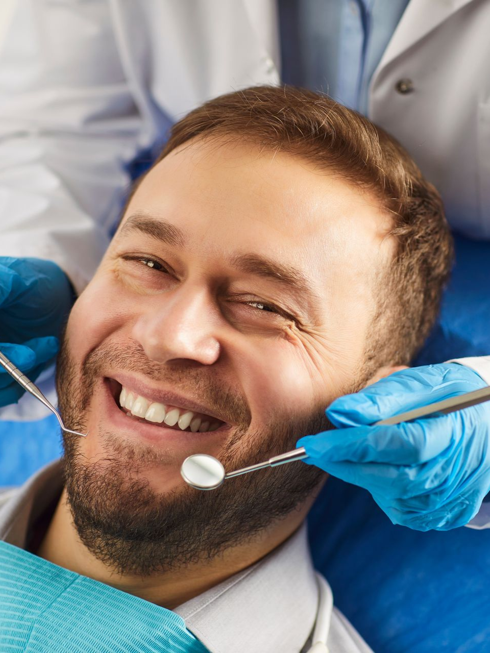 Smiling man receiving a dental exam with gloved hands and dental tools in a clinic