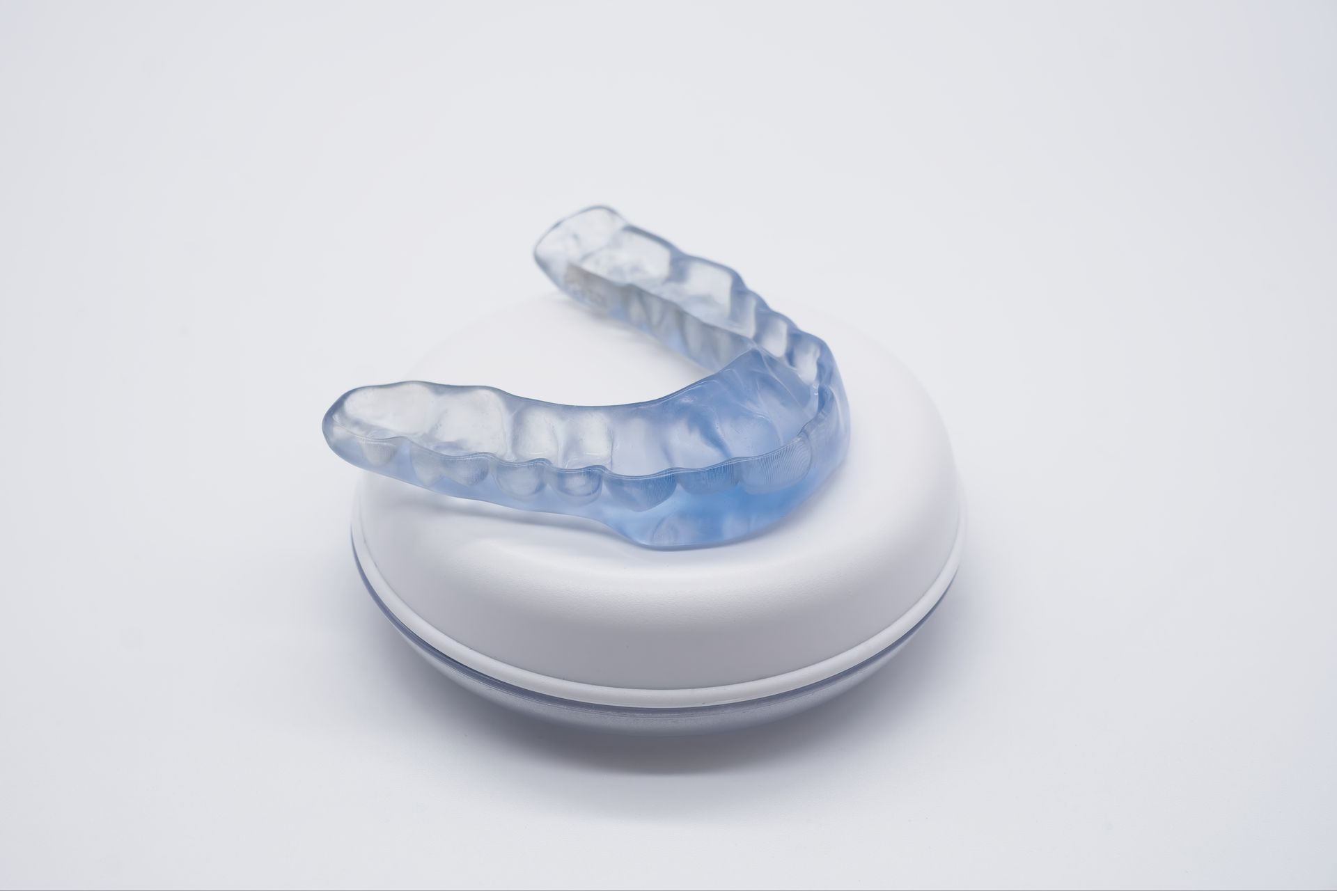 Transparent blue aligner on a white round case against a light background