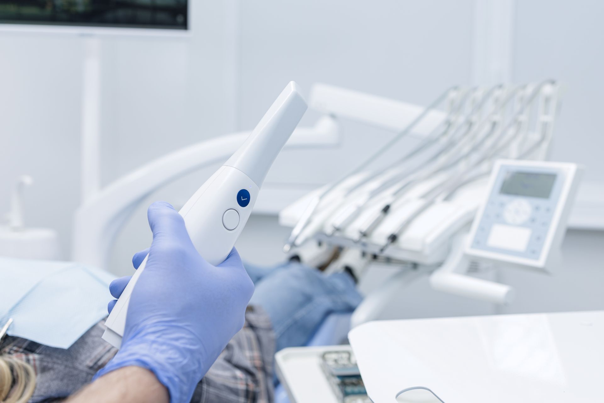 Dentist’s gloved hand holding a dental tool beside a patient chair in a bright clinic