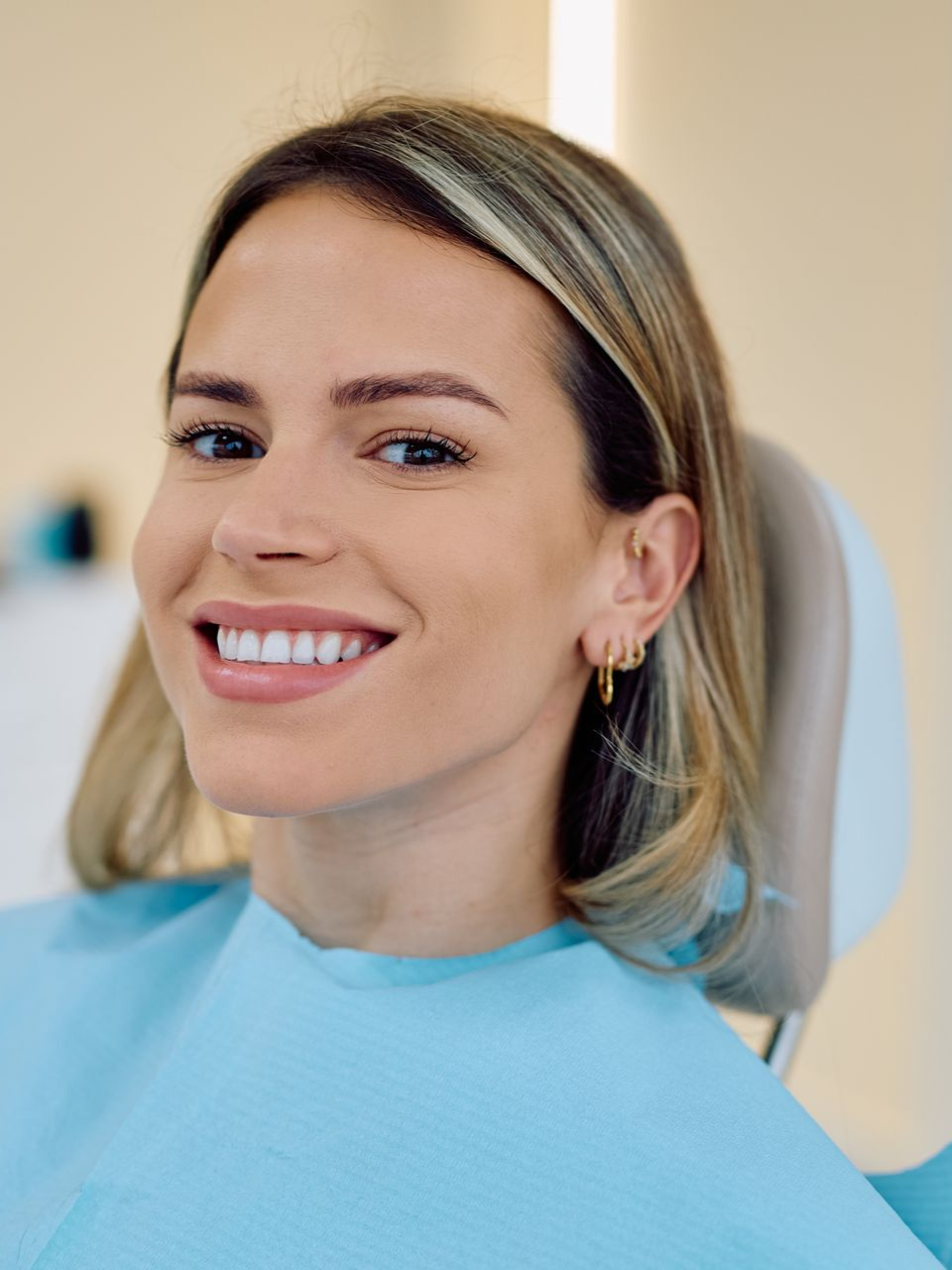 Smiling woman in a light blue top, seated indoors against a soft beige background