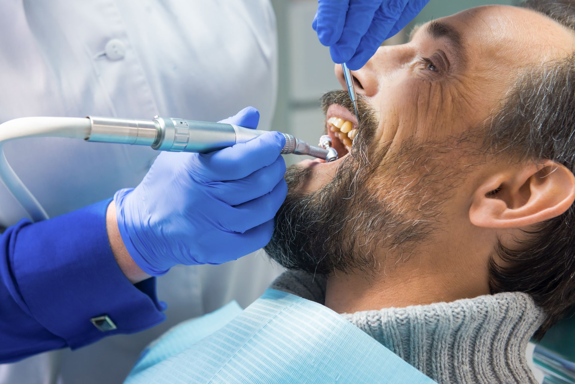 Dentist examining a patient’s mouth with dental tools and blue gloves in a clinic