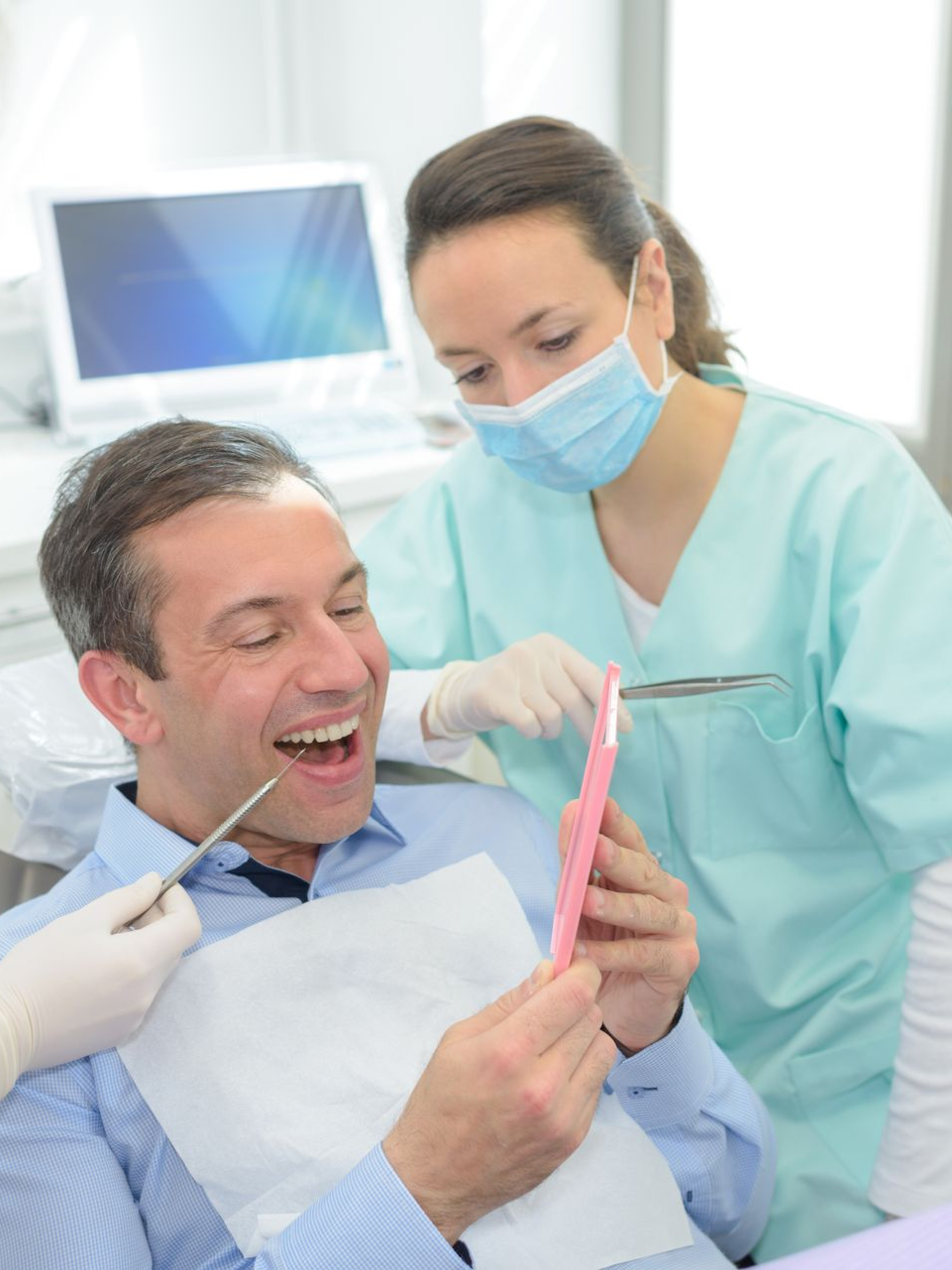 Dental hygienist examining a smiling patient with a mirror in a bright clinic