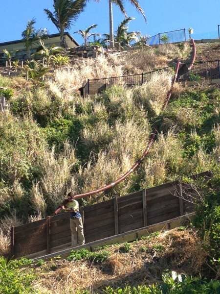 A Man Is Working On A Wooden Fence On A Hillside — Mulch, Fencing And Landscaping Mackay, QLD
