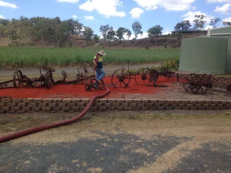 A Man Is Standing Next To A Hose In A Field — Mulch, Fencing And Landscaping Mackay, QLD