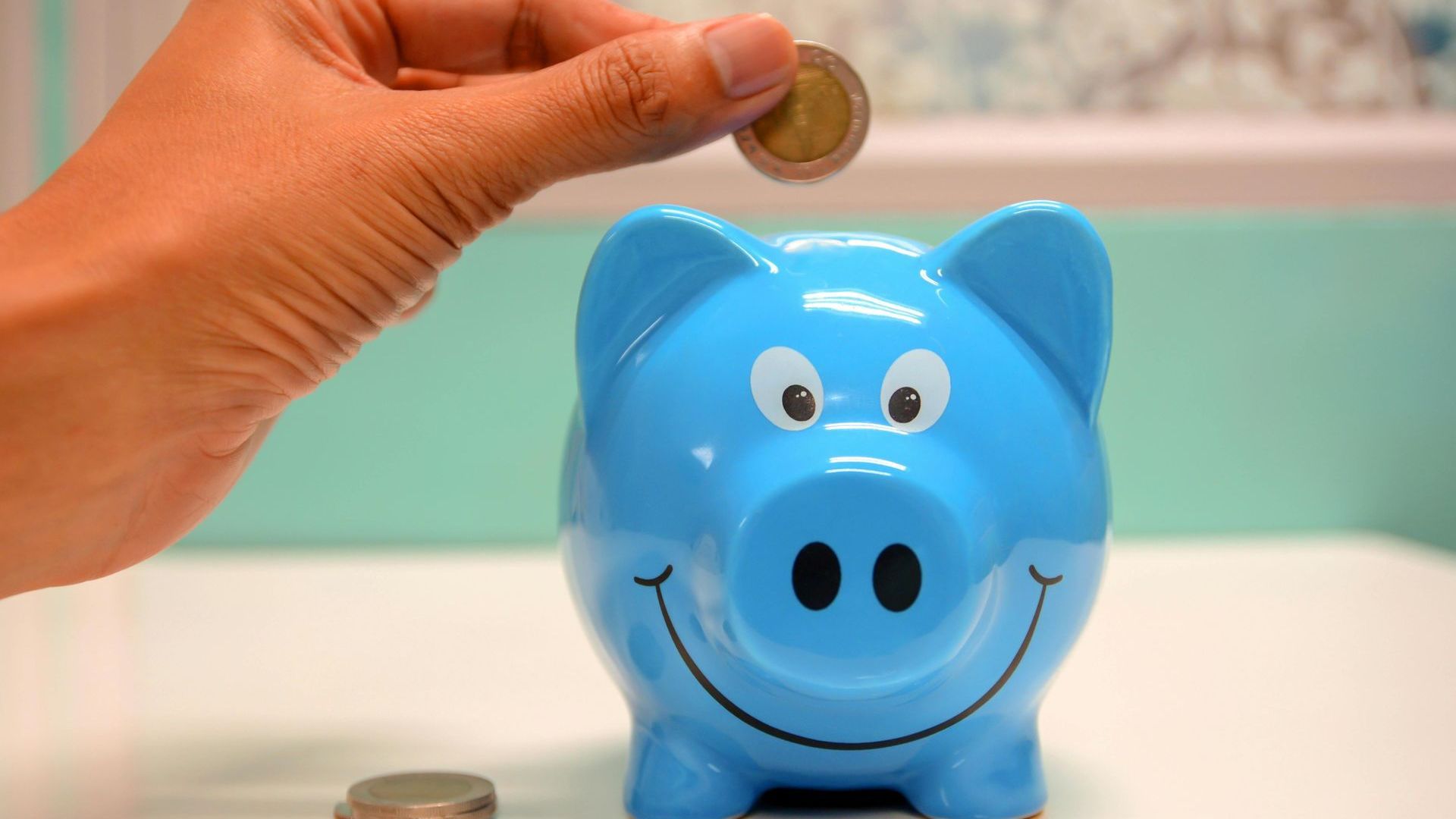 A person is putting a coin into a blue piggy bank.
