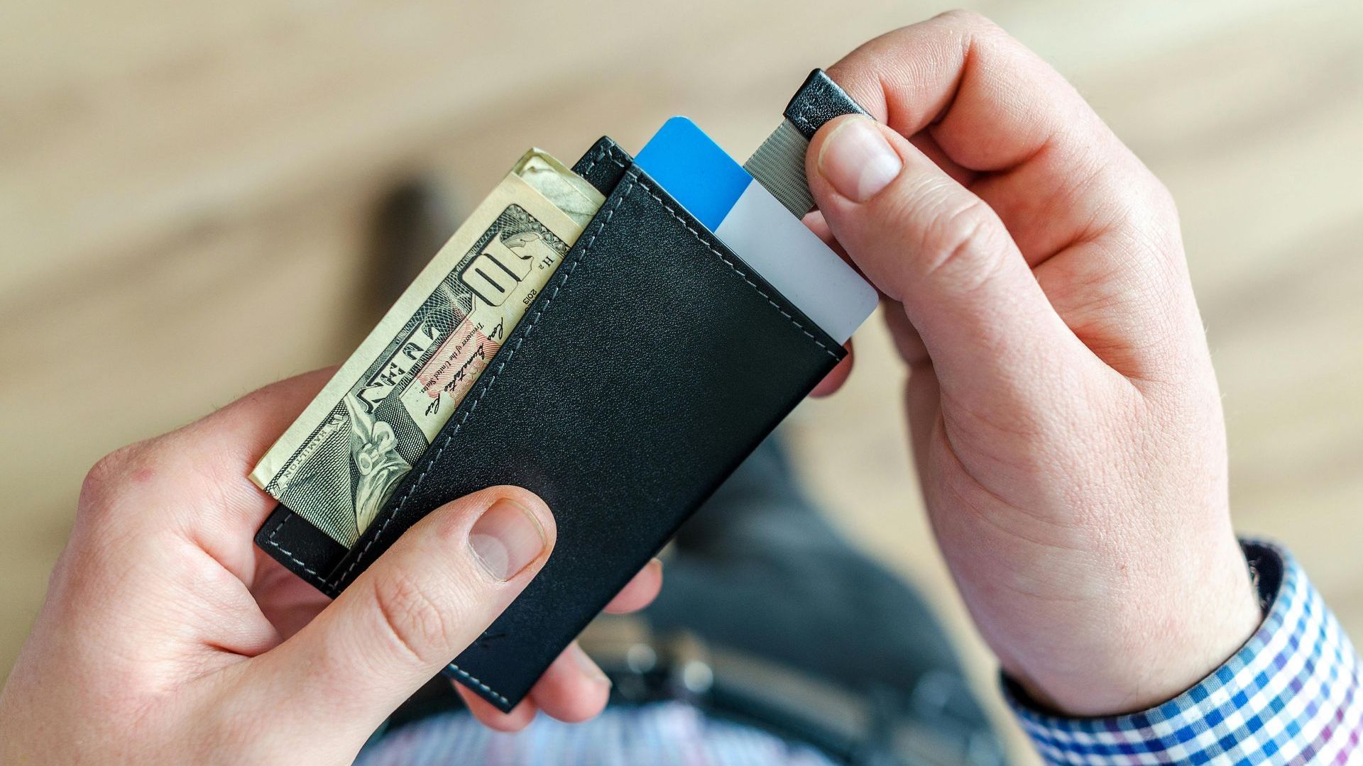 A person is holding a wallet with money and a credit card in it.